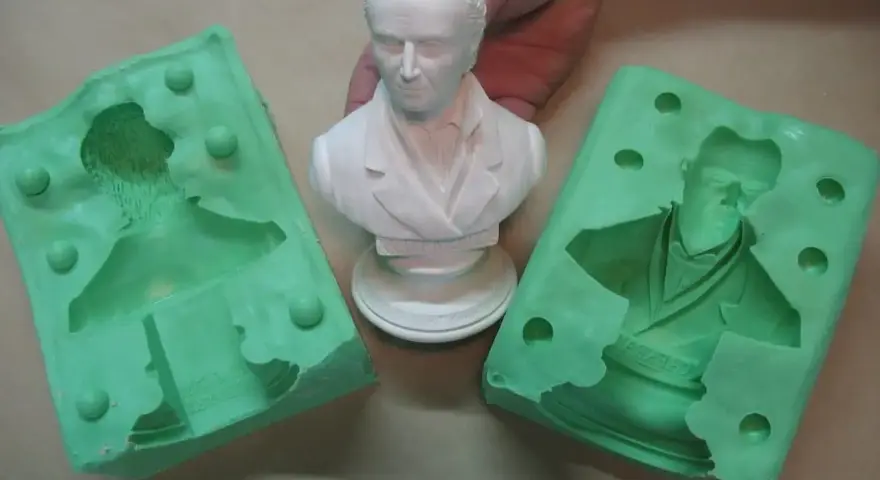 Making silicone molds for resin casting. A white bust is held between two green silicone molds, ready to capture its detail.
