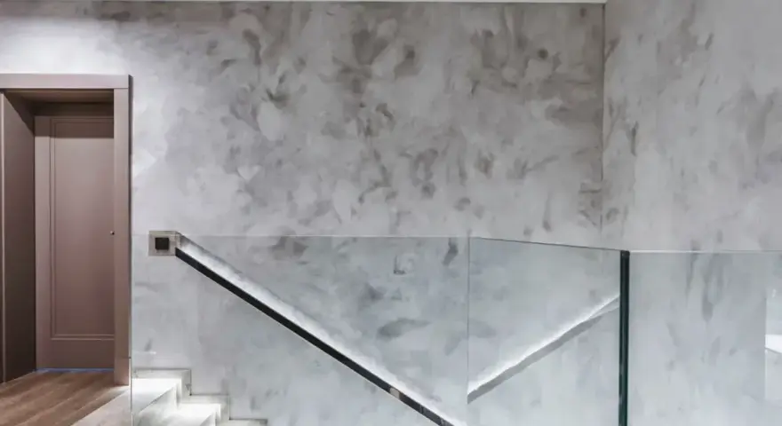 Nowoczesny hol z podświetlanymi schodami i szklaną balustradą. Efektowny tynk na ścianie dodaje wnętrzu elegancji.