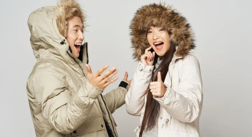 Pareja feliz con abrigos de invierno, ¡el mejor abrigo para el frío! Ella da pulgar arriba, él gesticula.