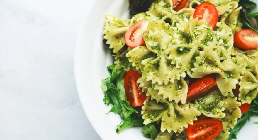 Pyszny makaron farfalle z aromatycznym pesto i soczystymi pomidorkami koktajlowymi, podany na liściach sałaty.