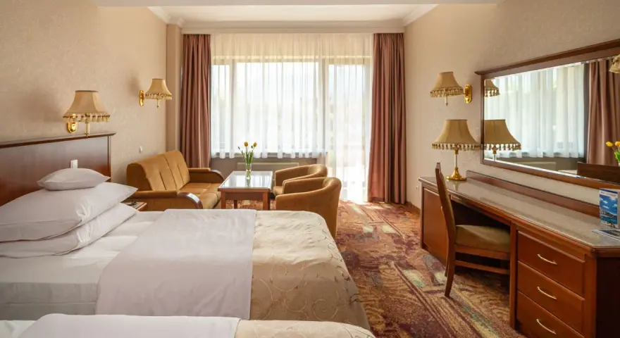 Pokój w Hotelu Gołębiewski Karpacz. Sprawdź cennik i zarezerwuj pobyt w tym przytulnym wnętrzu z dwoma łóżkami, kanapą i biurkiem.