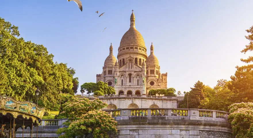 El barrio Montmartre, con la basílica del Sacré-Cœur al fondo, un carrusel y árboles frondosos bajo un cielo azul.
