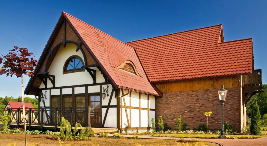 Elegancki dom z charakterystycznym dachem pokrytym czerwoną dachówką karpiówką, otoczony zadbanym ogrodem.