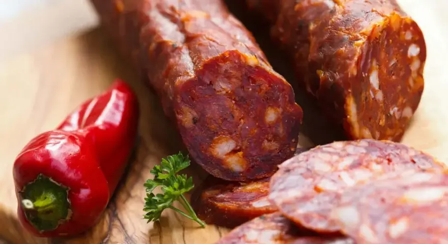 Kawałki pikantnego chorizo, czerwona papryczka i natka pietruszki na desce. Chorizo co to? To aromatyczna kiełbasa!