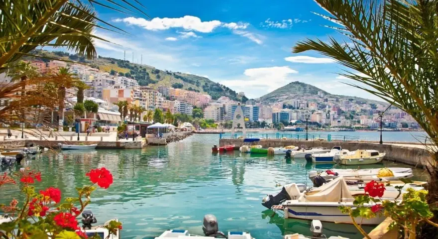 Piękne albania widoki: port z łodziami, palmy i kolorowe miasto na wzgórzu pod błękitnym niebem.