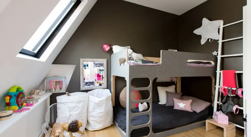 Accogliente camera da letto e cameretta insieme, con letto a castello grigio, giocattoli, cuscini a forma di stella e sacchi bianchi.
