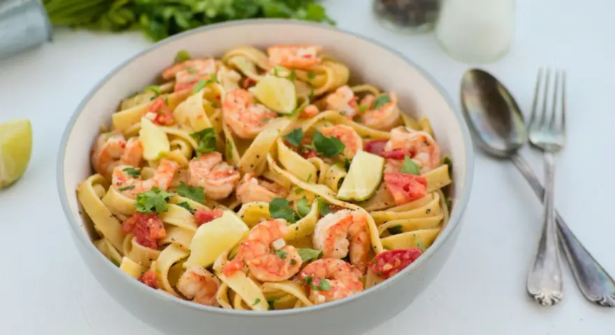 Pyszne tagliatelle z krewetkami, pomidorami i limonką, posypane świeżą natką pietruszki. Idealne danie na szybki obiad.