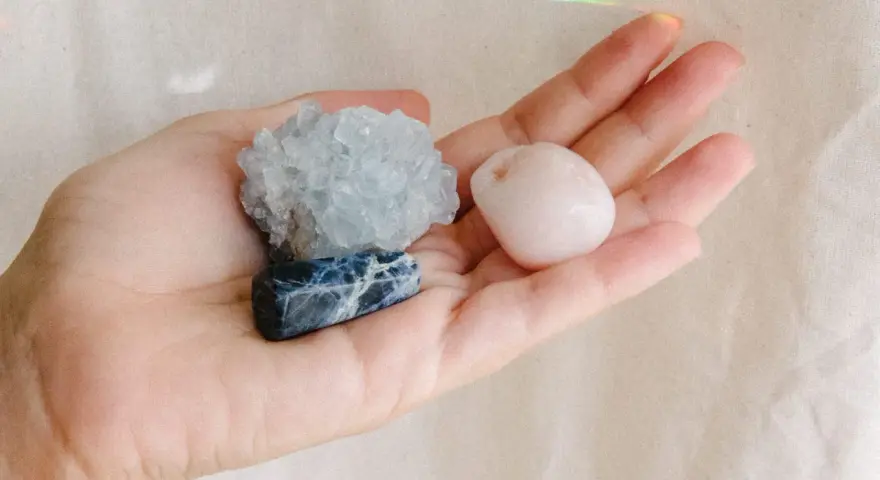 Mano sosteniendo tres piedras: una azul con vetas blancas, una azul pálido cristalina y una rosa pálido pulida. Son piedras para embarazadas.
