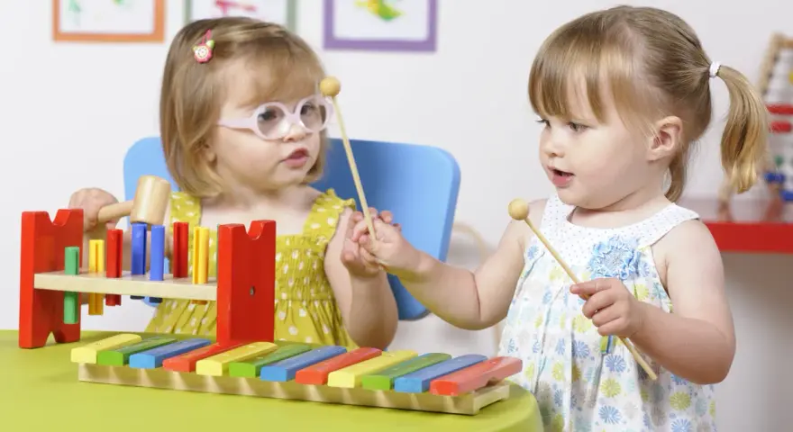 Deux petites filles s'amusent avec un xylophone, explorant la musique et les activités manuelles.