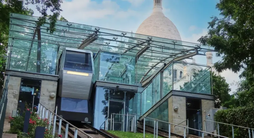 El funicular de Montmartre, con su moderna estación de cristal, asciende hacia la basílica del Sacré-Cœur bajo un cielo azul.