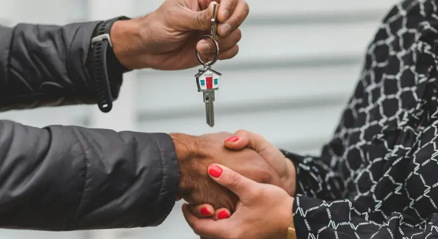 Une main tend une clé avec un porte-clés en forme de maison. Les deux mains se serrent, symbolisant la fin d'une obligation de relogement par la mairie.