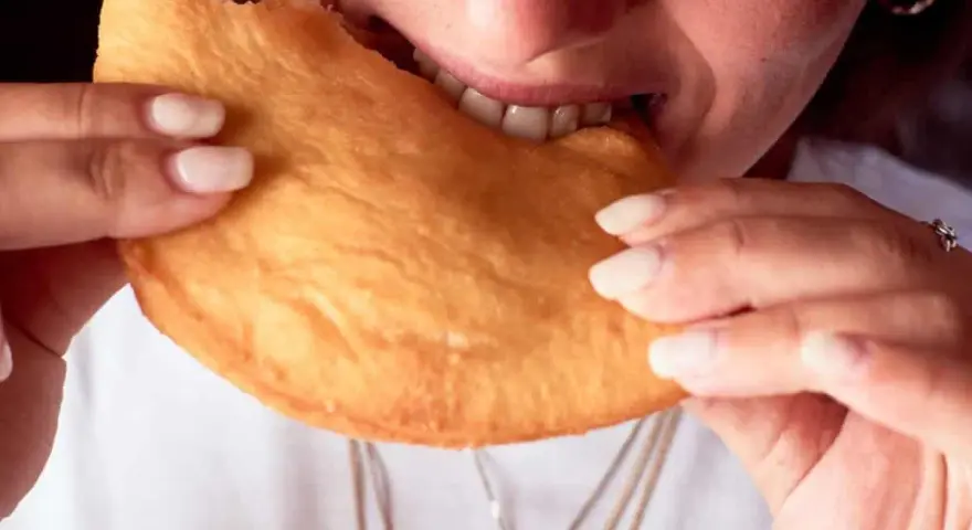 Close-up of a person biting into a golden-brown, fried pastry.