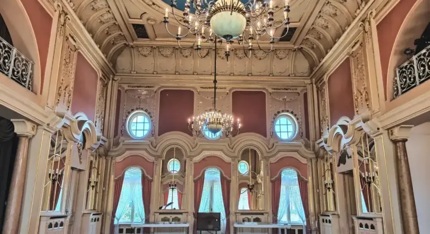 Wnętrze pałacu w Poznaniu, idealne do zwiedzania. Bogato zdobiony sufit, kryształowe żyrandole i eleganckie zasłony tworzą atmosferę dawnej świetności.