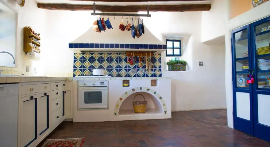 Cocina rústica con azulejos coloridos y detalles DIY, ideal para decorar casa de campo con poco dinero. Cestas y ollas cuelgan, creando un ambiente acogedor.