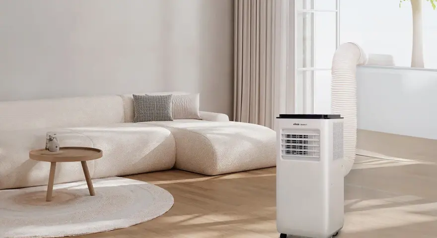 Un aire acondicionado portátil con tubo de escape conectado a la ventana, parte de unas modernas instalaciones hvac, en un salón con sofá beige.