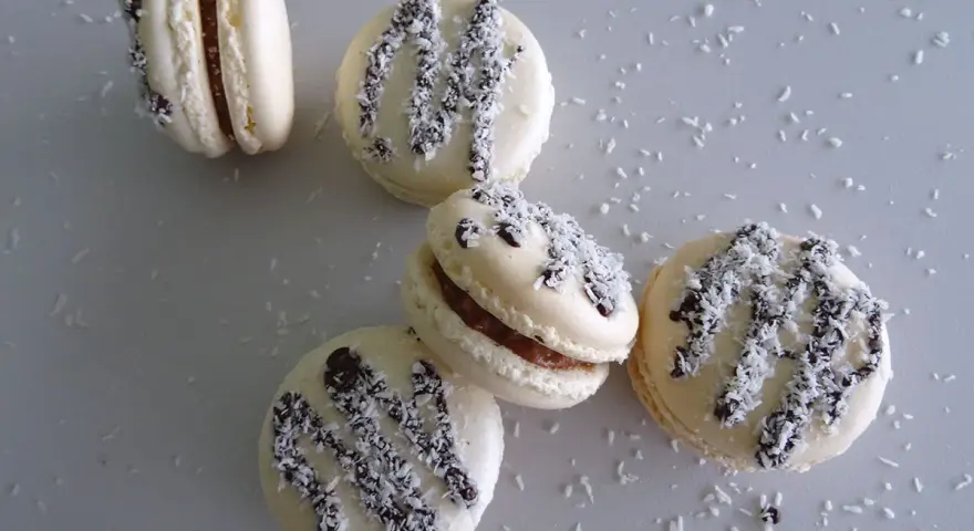 Macarons à la ganache coco, parsemés de noix de coco râpée et de copeaux de chocolat noir.
