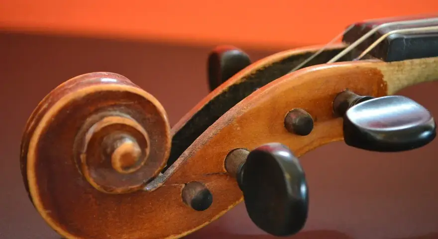 Drewniana ślimacznica skrzypiec, przypominająca spiralę, symbolizuje pierwsze instrumenty muzyczne i ich prostotę.