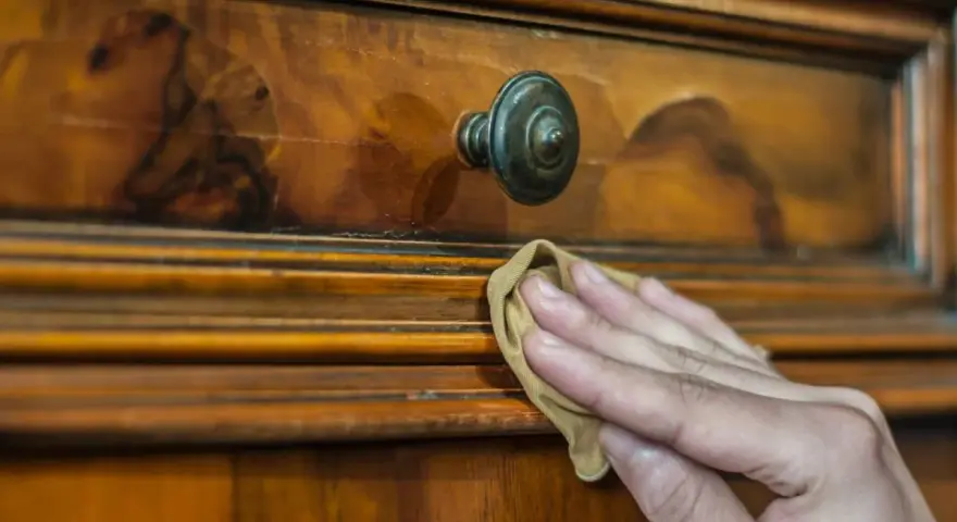Restauración de mueble antiguo. Mano aplicando betún de judea antes y después, revelando su brillo natural.