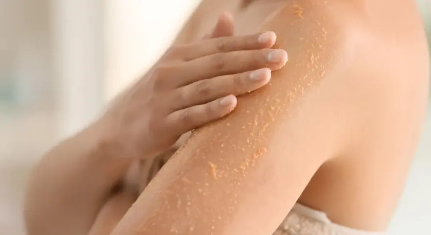Mano che applica scrub su braccio, rimuovendo la pelle morta dopo la doccia per una pelle liscia e luminosa.