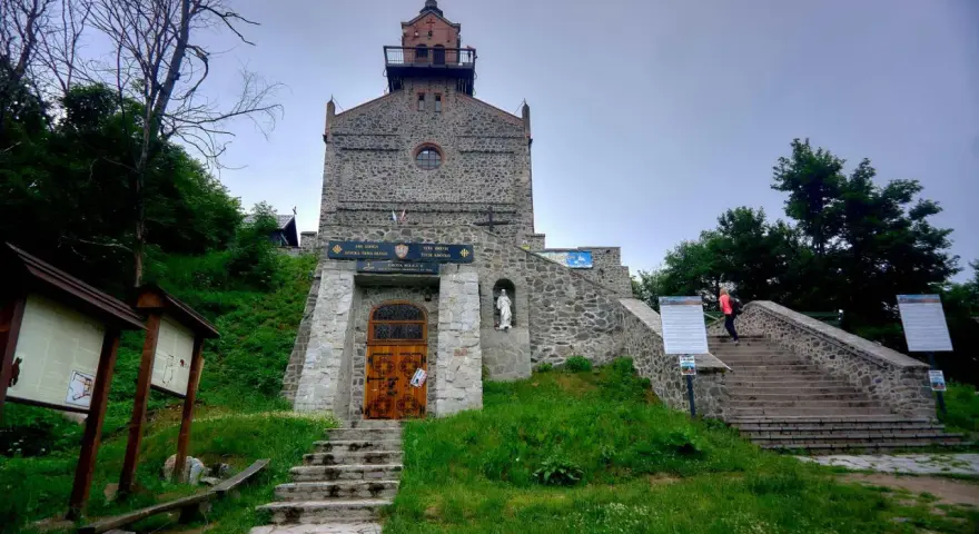 Kamienna wieża na górze Ślęża, z kamiennymi schodami prowadzącymi do wejścia. Wokół zieleń i drzewa.