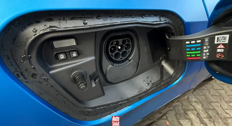 Gniazdo ładowania w niebieskim samochodzie. To pokazuje, co to jest plug-in hybrid – samochód, który można ładować z sieci.