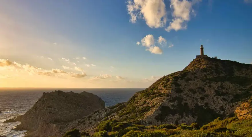 Faro solitario su una collina rocciosa, con il mare e le nuvole al tramonto. Un paesaggio mozzafiato di Nebida, Sardegna.