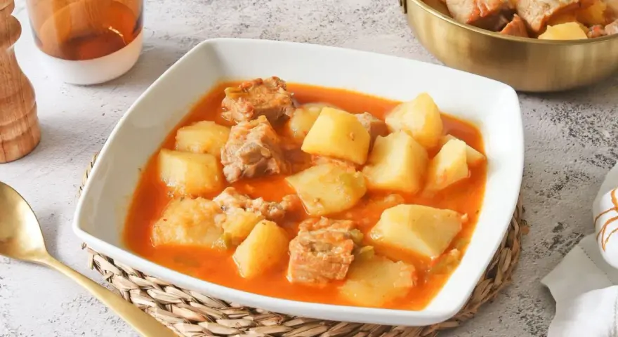 Un reconfortante plato de patatas con costillas en una salsa rojiza, servido en un cuenco blanco.