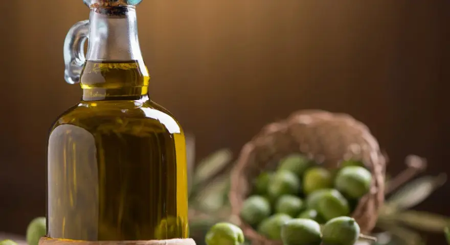 Bottiglia di olio extravergine d'oliva accanto a olive verdi, per capire la differenza tra olio di oliva e olio extravergine.