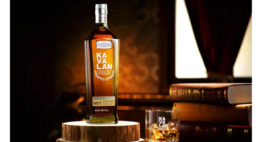 Butelka Kavalan Single Malt Whisky, uznawana za najlepszą polską whisky, obok szklanki z lodem i sterty książek.