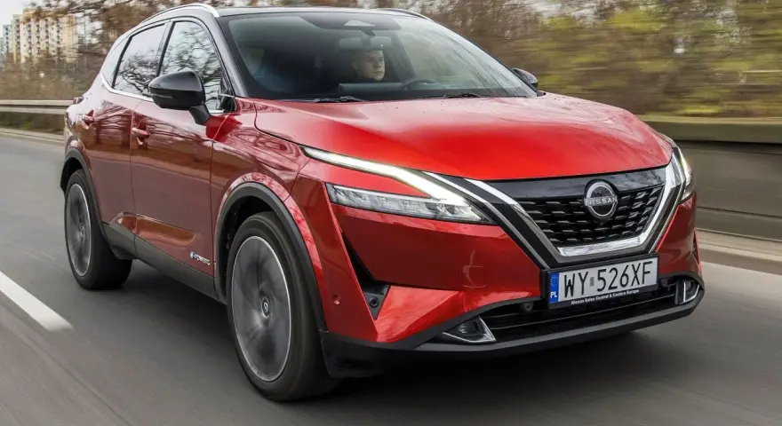Czerwony Nissan Qashqai 2023 z napędem e-POWER jedzie po drodze, za kierownicą siedzi kierowca.