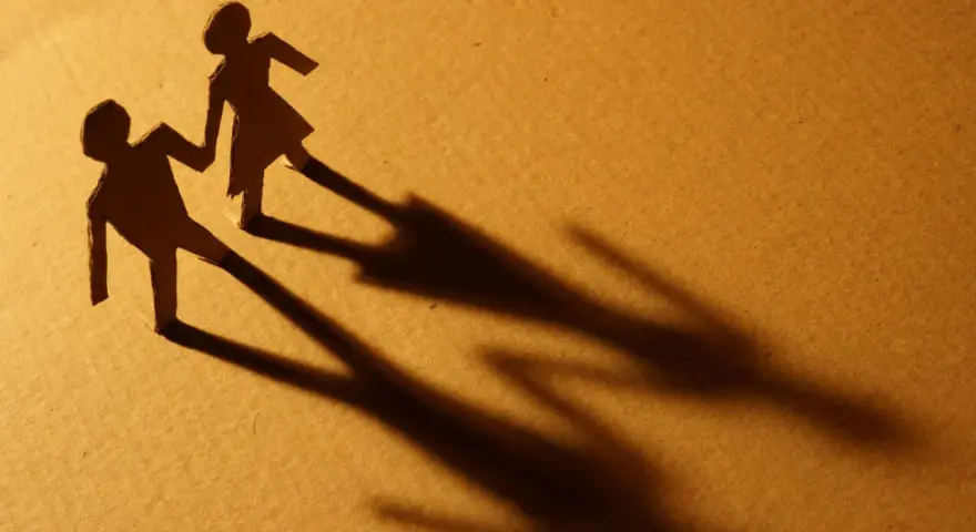 Zwei Papierfiguren, die sich an den Händen halten. Eine Figur scheint sich abzuwenden, während die andere bleibt. Sie sind noch verheiratet und eine neue Beziehung beginnt.