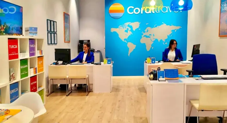 Biuro podróży Coral Travel z pracownicami za ladą i mapą świata na ścianie.