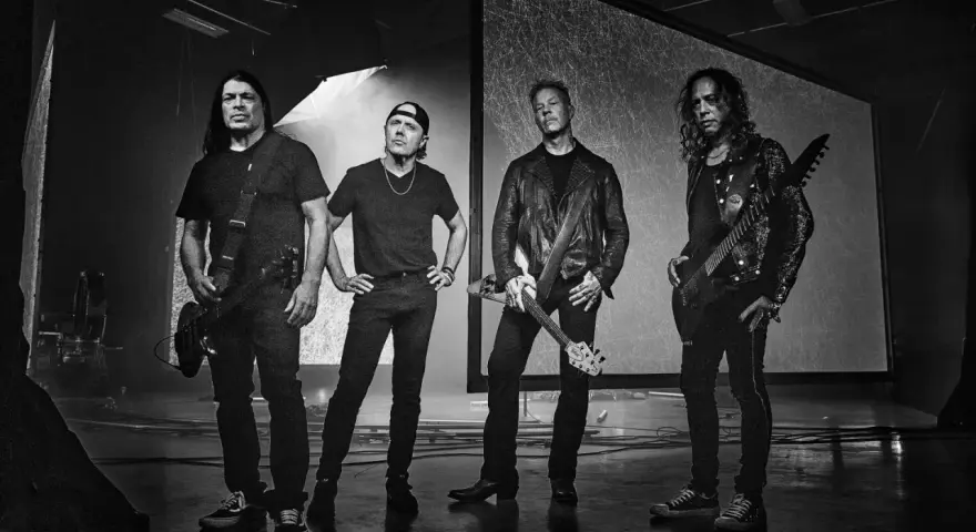 James Hetfield und Metallica im Jahr 2000, bereit für die Bühne. Die Bandmitglieder stehen in dunkler Kleidung, einige mit Gitarren.