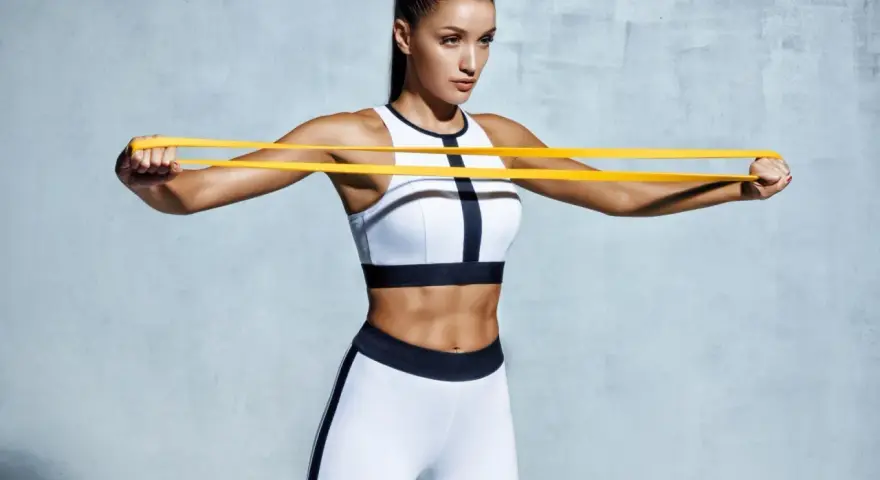 Femme athlétique travaillant ses pectoraux avec un élastique jaune.