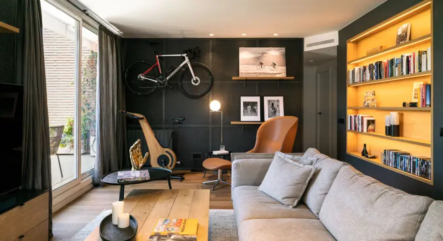 Un salón moderno con bicicleta de carretera colgada, máquina de ciclismo de madera y estanterías iluminadas. Inspiración decoración para deportistas.