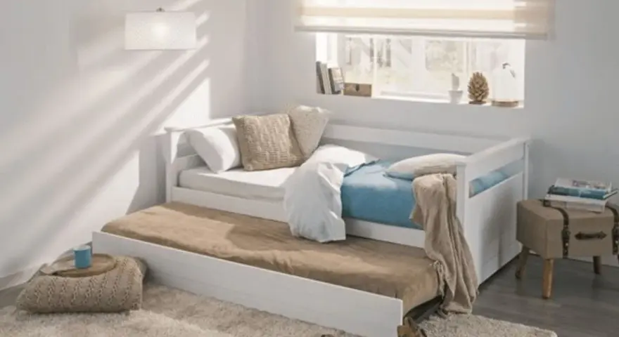 Cama nido blanca con colchones, cojines y manta en un dormitorio juvenil.