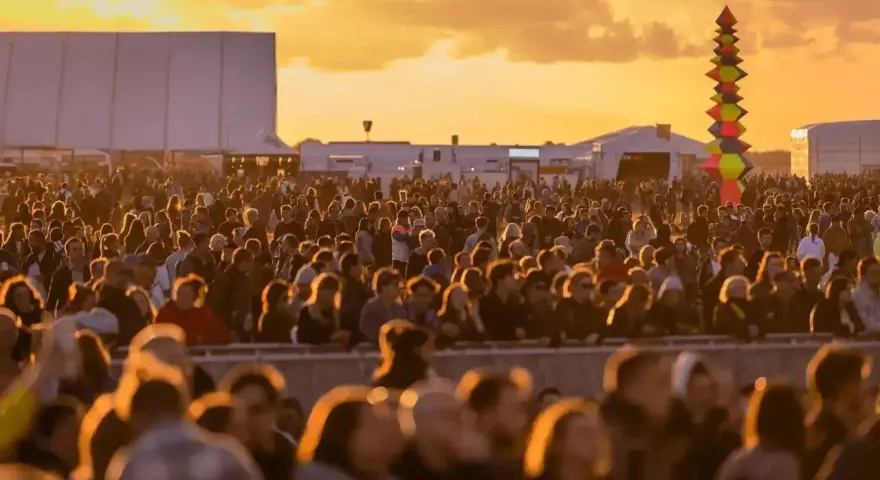 Tłum ludzi na festiwalu, zachód słońca. Kolorowa instalacja artystyczna w tle. Kto będzie następny na scenie?