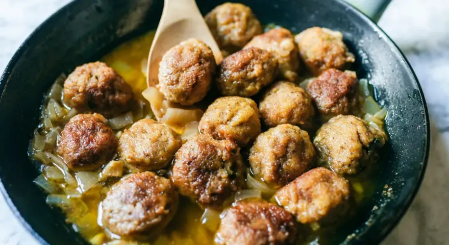 Polpette in bianco dorate e succulente, cotte in padella con cipolle dolci e un sughetto invitante.