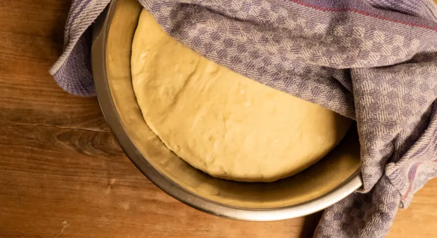 Ein geschmeidiger Teig ruht in einer Schüssel, bedeckt mit einem karierten Tuch, bereit für das Backen.