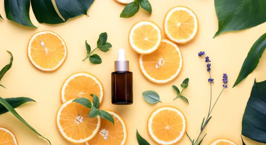 Siero viso con niacinamide e acido glicolico, circondato da fette d'arancia, foglie verdi e lavanda.
