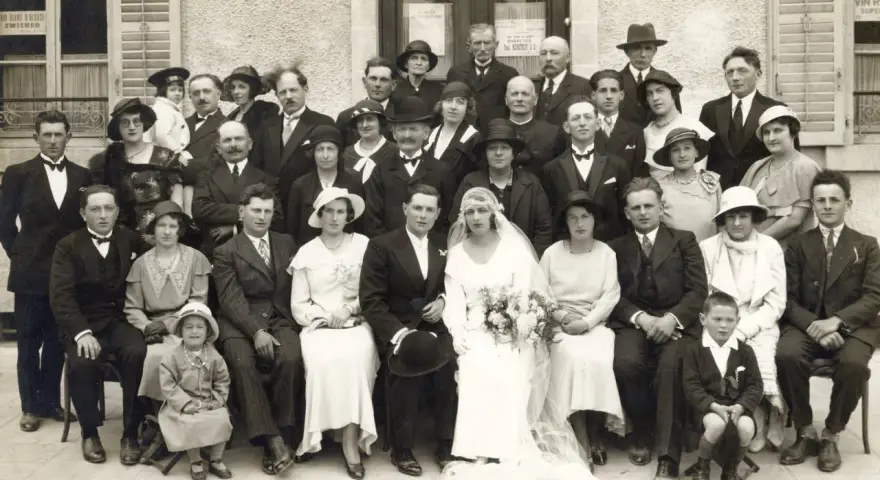 Un groupe pose pour une photo de mariage, peut-être pour un registre mariage. La mariée porte une robe blanche et un voile.