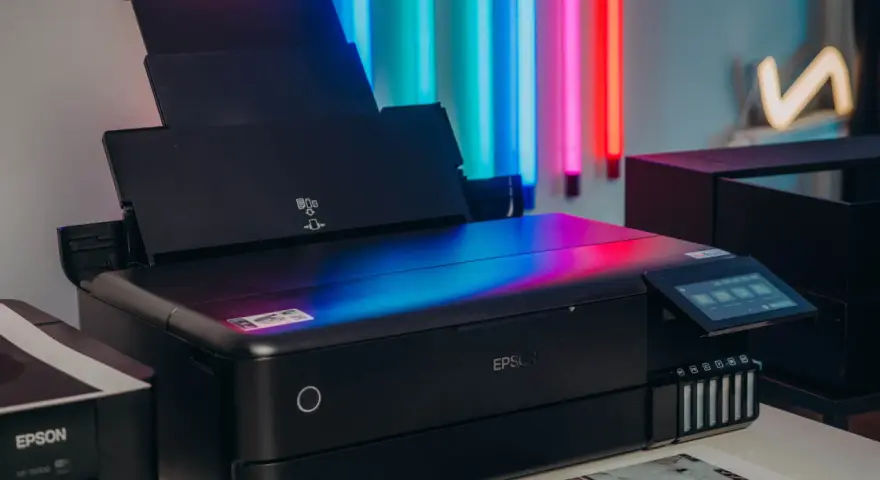 Czarna drukarka Epson z kolorowym ekranem, idealna do drukowania zdjęć. Obok stoi starszy model.