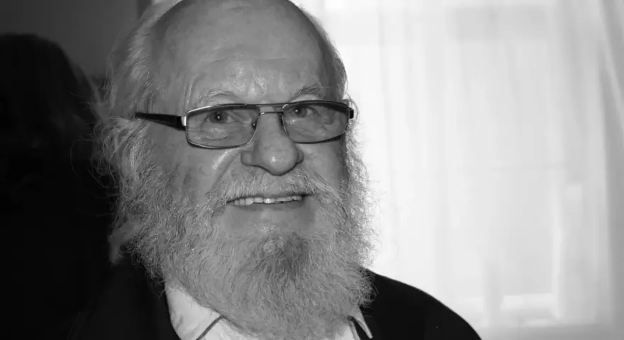 Uśmiechnięty Aleksander Skowroński z siwą brodą i okularami.