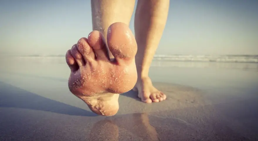 Paluch biegacza pokryty piaskiem, stopy na mokrym piasku przy plaży.