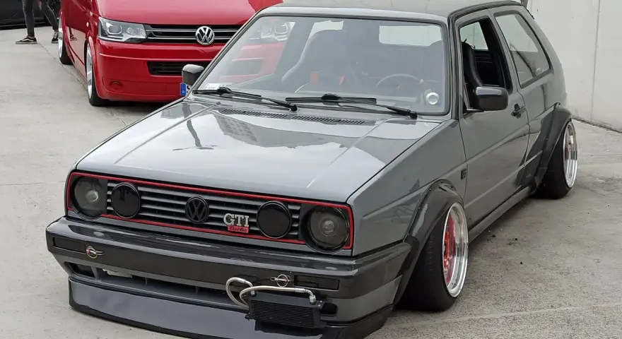 Szary, zmodyfikowany Volkswagen Golf GTI z szerokimi błotnikami i spojlerem.