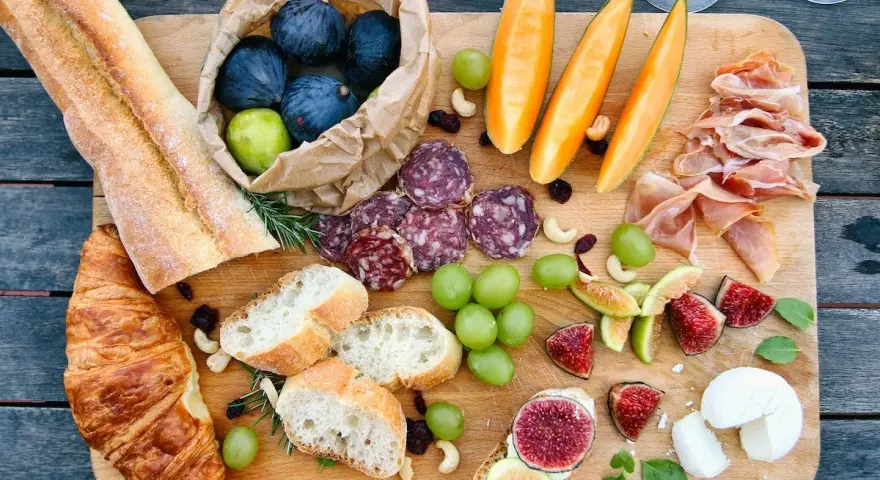 Tabla de quesos y embutidos: baguettes, croissants, higos, uvas, melón, jamón serrano y salami. Un festín que muestra qué comen los franceses.