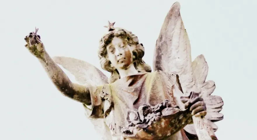 Kamienna figura anioła z gwiazdą na głowie, trzymająca w dłoniach kwiaty i gałązkę. Symbolika 2244 znaczenie.