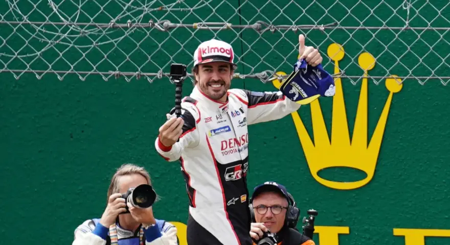 Fernando Alonso celebra su victoria en Le Mans, con una gorra y un trofeo. Fotógrafos capturan el momento.