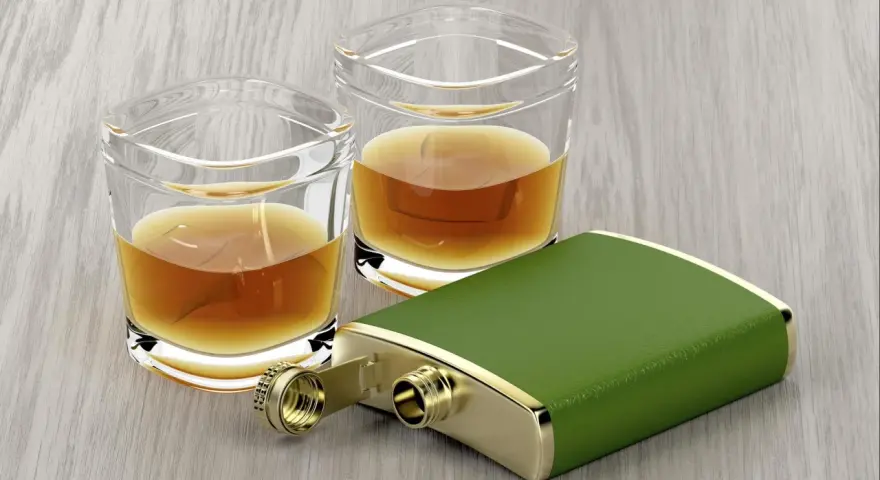 Zwei Gläser mit bernsteinfarbenem Whiskey und ein grüner Taschenflachmann. Ein 4 cl Whiskey hat ca. 90 Kalorien.