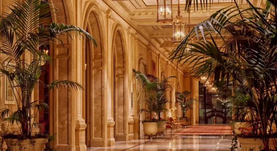 Elegancki korytarz z łukami i palmami, przypominający wnętrze najdroższego hotelu na świecie.